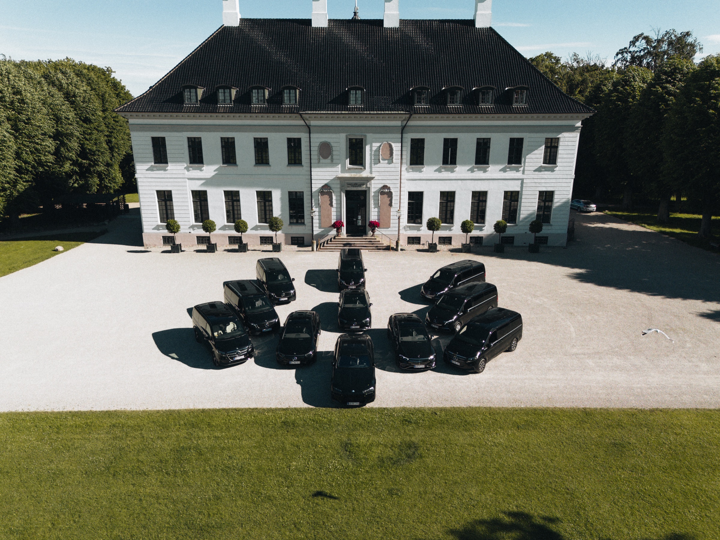 The LuxLimo chauffeur fleet of electric Mercedes-Benz and BMW cars lined up at a Danish manor house, seen from above